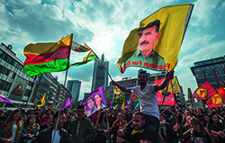 Abgebildet sind Demonstrationsteilnehmer in Frankfurt am Main, die Fahnen von Organisationen zeigen, die der Arbeiterpartei Kurdistans nahestehen. Im Vordergrund ist eine Fahne mit dem Konterfei Abdullah Öcalans zu erkennen.